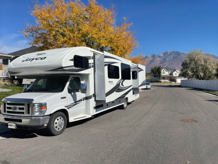 White Jayco RV rental with slide-outs extended, parked on an autumn street with mountains in the background.. Jayco Greyhawk 2018