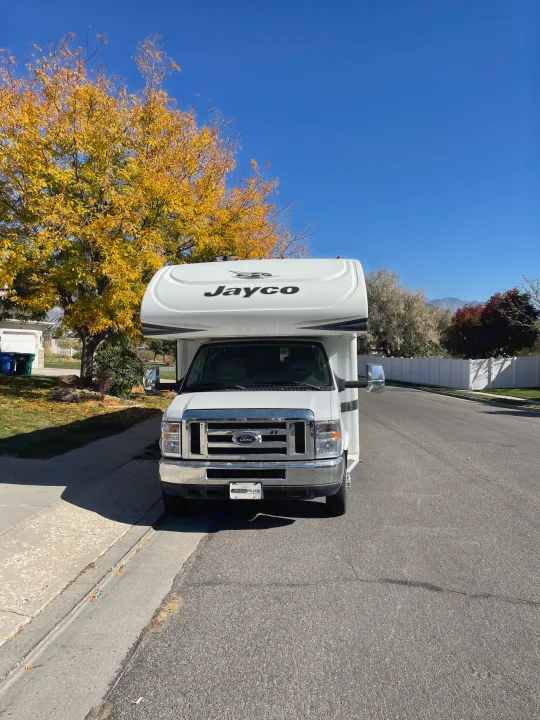 White Jayco RV rental parked on a residential street under a blue sky with vibrant autumn trees.. Jayco Greyhawk 2018