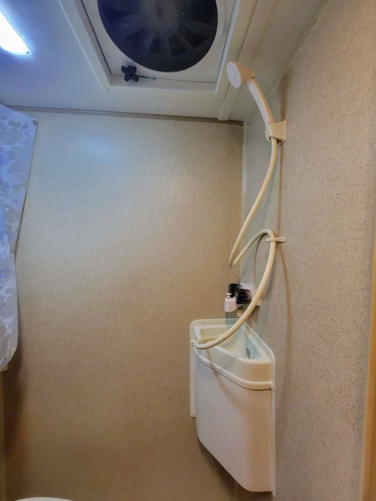 Inside an RV rental's compact wet bath, featuring a handheld shower, corner sink with faucet, and ceiling vent fan.. R-Pod R-Pod Trailer 2015