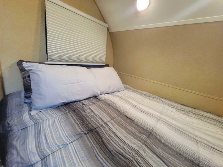 Cozy RV rental bedroom featuring a striped bed with two pillows and a pleated window blind.. R-Pod R-Pod Trailer 2015