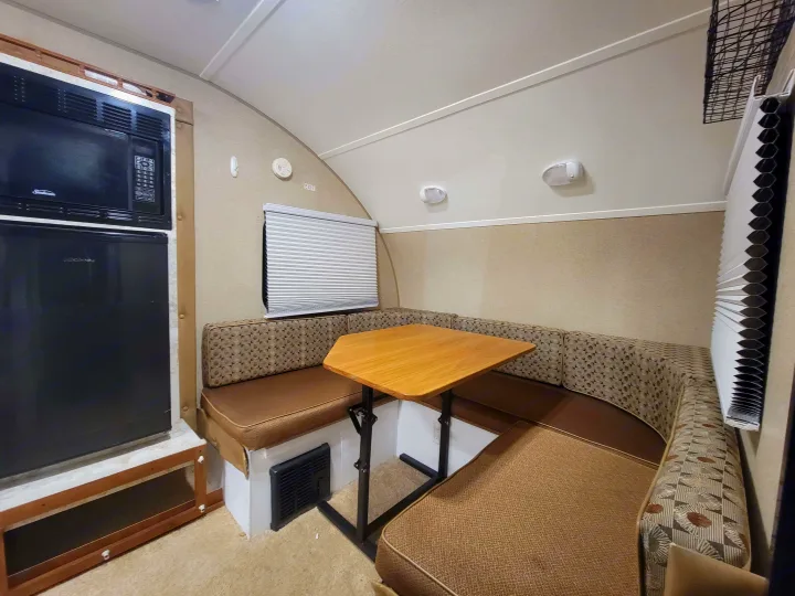 RV rental interior showcasing a U-shaped dinette with brown cushioned seating, wood table, microwave, and fridge.. R-Pod R-Pod Trailer 2015