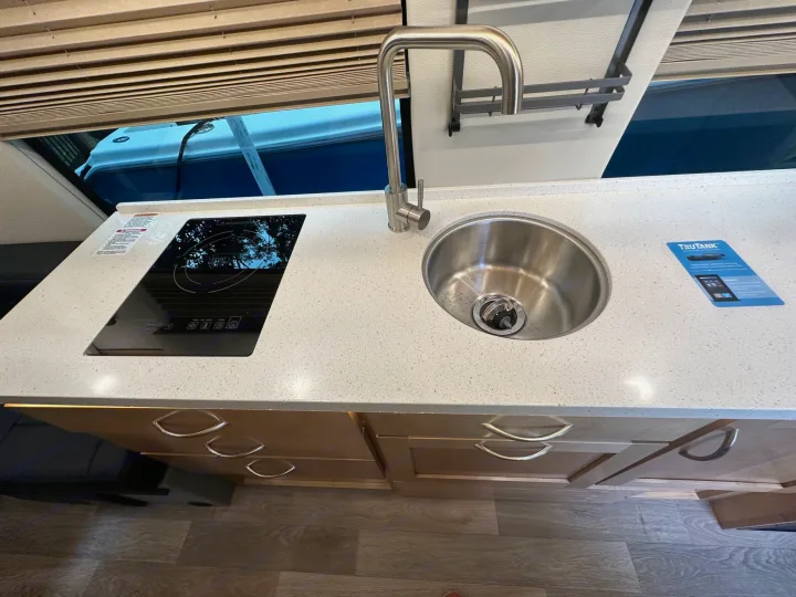 RV rental kitchen featuring a sleek induction cooktop, stainless steel sink, and light wood cabinetry.. Coachmen Other 2022