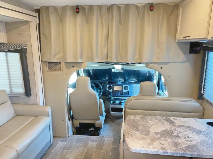 RV rental interior looking toward the cab. Features include comfy seating, a dash sunshade, and an overhead bunk.. Thor Chateau 2022