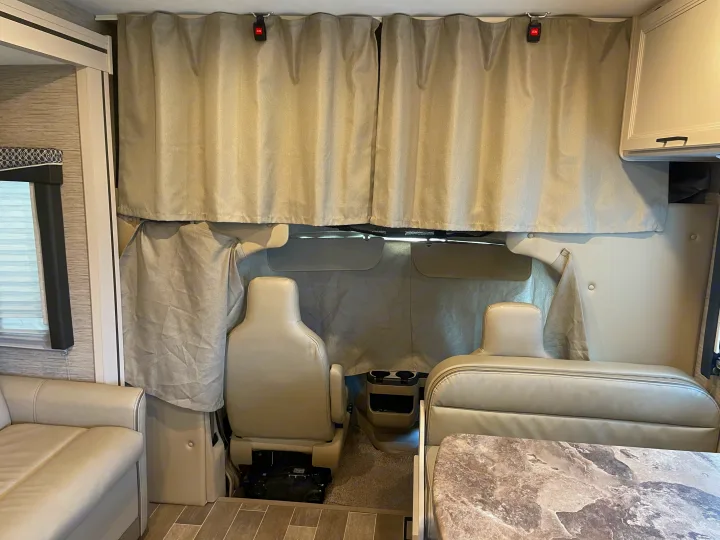 Inside an RV rental: front cabin with two swivel seats, privacy curtains, and a nearby dinette and sofa.. Thor Chateau 2022
