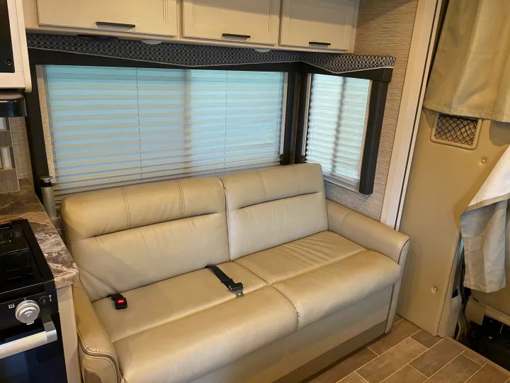 Modern RV rental interior: cozy sofa with seatbelts, large windows, and overhead cabinets for comfortable travel.. Thor Chateau 2022
