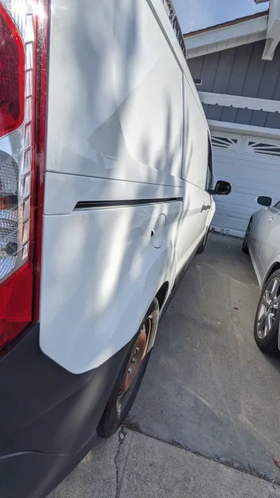 White RV rental van, passenger side and rear view, parked in a driveway with another vehicle nearby.. Ford Transit Custom 2017