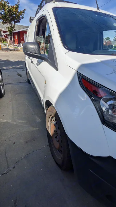 A white van, often used for RV rental conversions, displays its front side, roof rack, and carbon fiber mirror.. Ford Transit Custom 2017