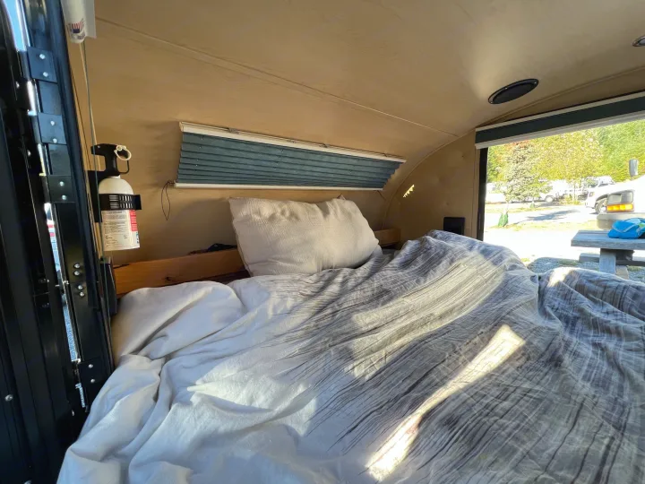 View inside a cozy rv rental with a made bed, window with blinds, and fire extinguisher by the door.. Little Guy Silver Shadow 2016