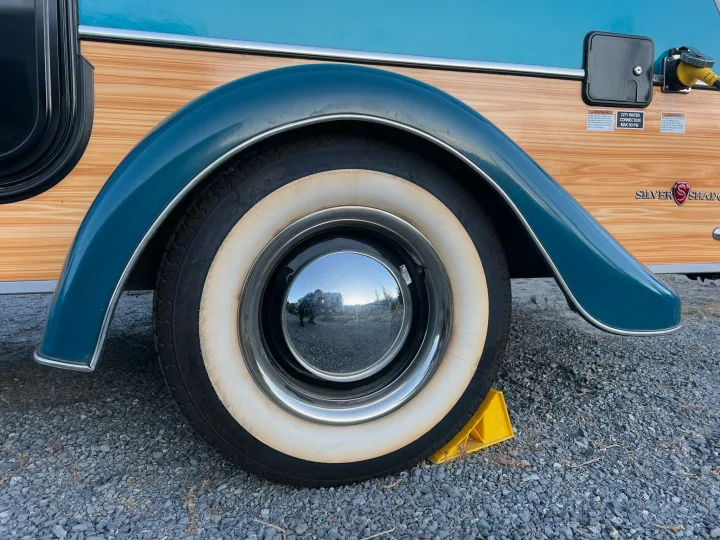 A retro RV rental on gravel, featuring wood-grain siding, a blue fender, whitewall tire, and utility panel.. Little Guy Silver Shadow 2016