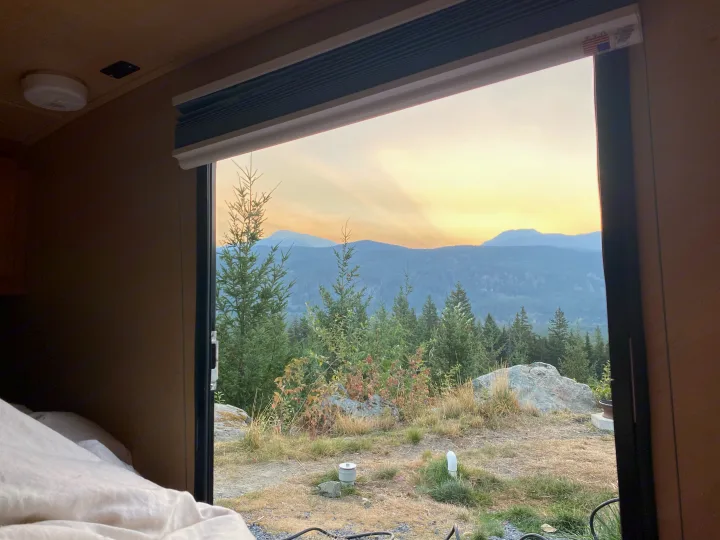 A peaceful mountain and forest view from an RV rental, with a golden sky at dawn or dusk, seen from the cozy interior.. Little Guy Silver Shadow 2016