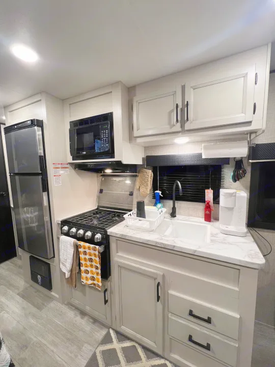 RV rental kitchen featuring a fridge, microwave, stove, sink, light cabinetry, and marble-look counters.. Jayco Jay Flight SLX 2022