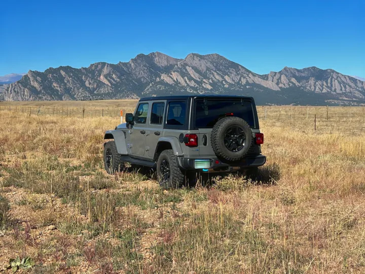 Gray Jeep Wrangler in a field with mountains. Great for exploring where RV rentals can't go.. Jeep Wrangler 2022
