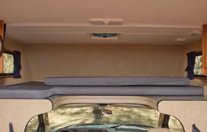 Inside an RV rental: view of the comfortable over-cab bed area with striped cushions, side windows, and ceiling vent.. Thor Majestic 2015