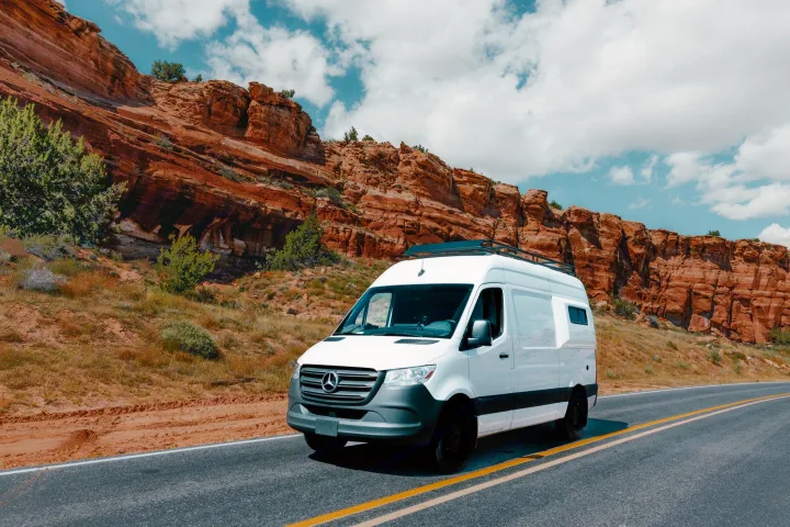 White Mercedes Sprinter van, likely an RV rental, on a desert road with stunning red rock formations.. Mercedes-Benz Sprinter RV Motorhome Campervan 2022
