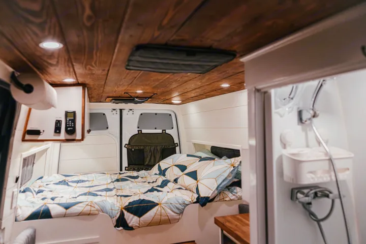 Cozy RV rental interior: bed with patterned duvet, wooden ceiling, and compact shower. Ideal for van life.. Mercedes-Benz Sprinter RV Motorhome Campervan 2022