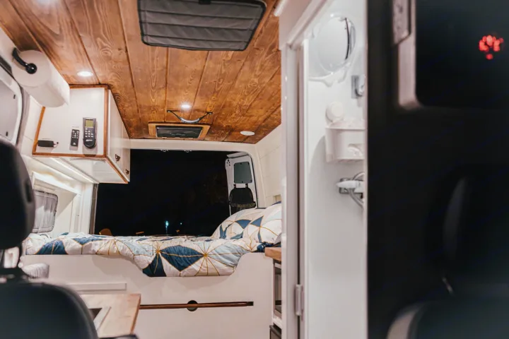 Relax in this RV rental's cozy interior: wood-paneled ceiling, comfy bed with geometric duvet, and integrated controls.. Mercedes-Benz Sprinter RV Motorhome Campervan 2022