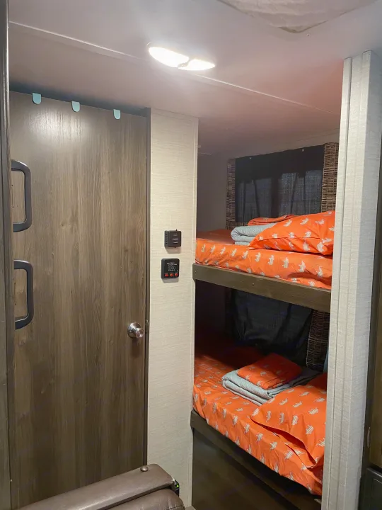 Cozy RV rental interior featuring bunk beds with orange bedding, a door, and control panels. Ideal for families on the go.. Keystone Bullet 2018