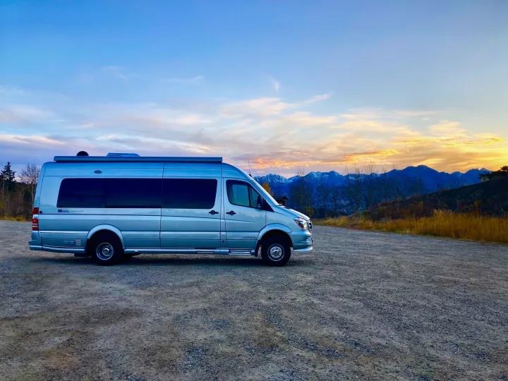 Silver Airstream Interstate rv rental van on gravel. Scenic mountains & vibrant sunset sky in background for your next adventure.. Airstream Interstate 2017