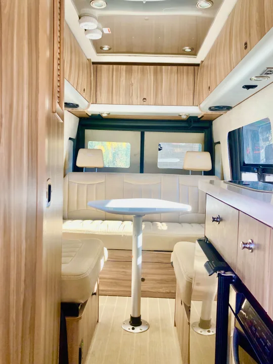Bright RV rental interior featuring a cream-colored dining area with a table, bench, and two seats, surrounded by light wood cabinetry.. Airstream Interstate 2017