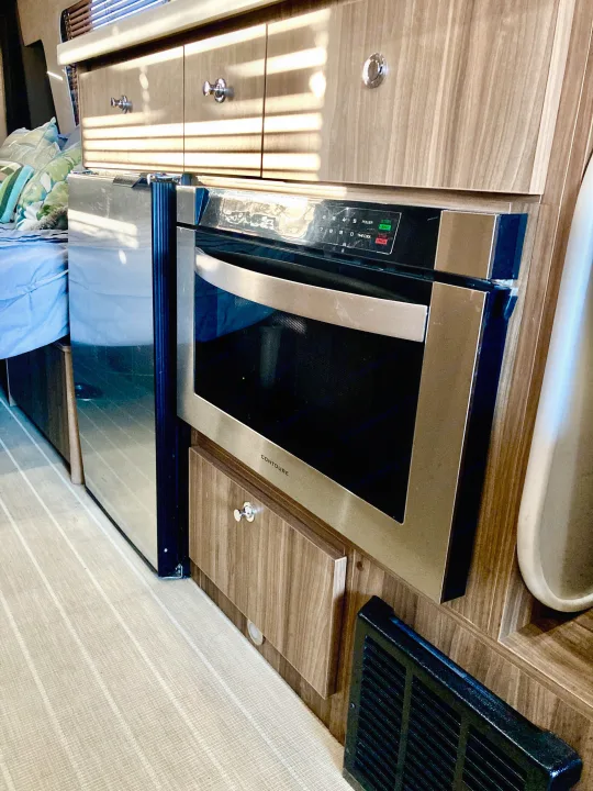 Compact RV rental kitchenette with a built-in CONTOURE microwave, refrigerator, and wood cabinets.. Airstream Interstate 2017