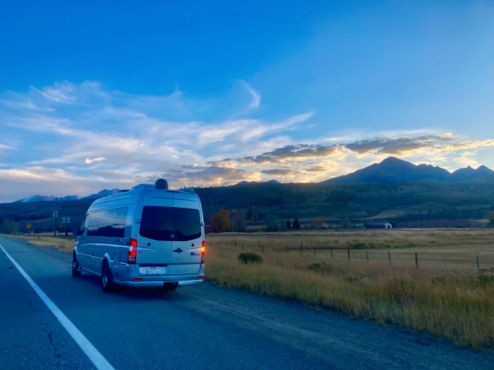 Grey Airstream RV rental parked on a road, bathed in sunset glow with scenic mountains and golden clouds.. Airstream Interstate 2017