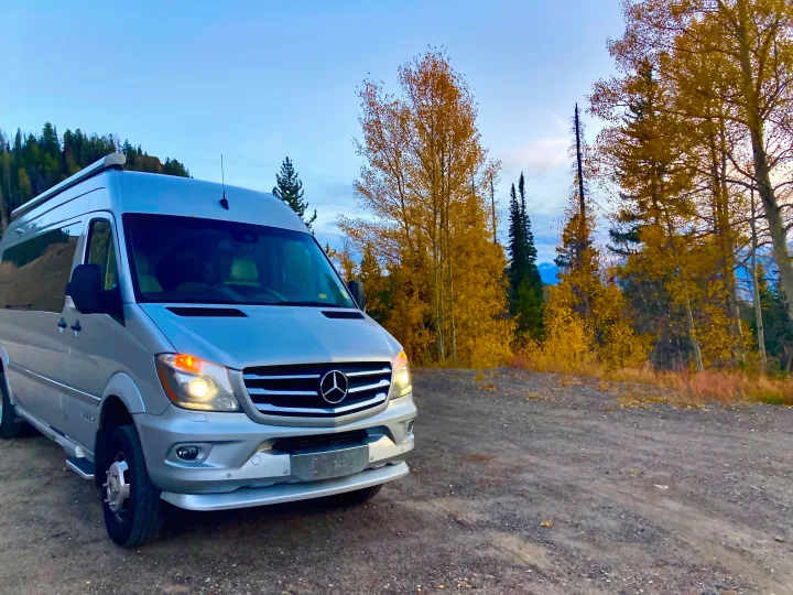 Silver Mercedes Sprinter camper van, perfect for an RV rental, set on a dirt road surrounded by vibrant autumn trees.. Airstream Interstate 2017