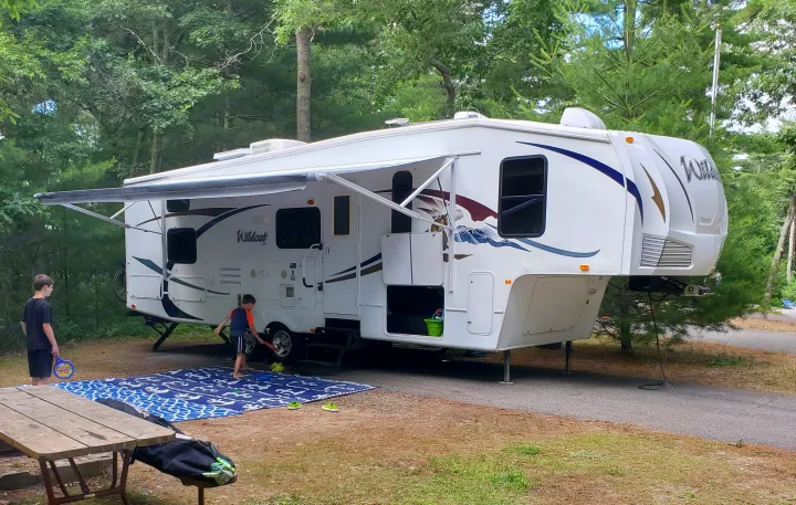 A spacious Wildcat fifth-wheel RV rental is set up at a wooded campsite, with children playing on a mat.. Forest River Wildcat 2009