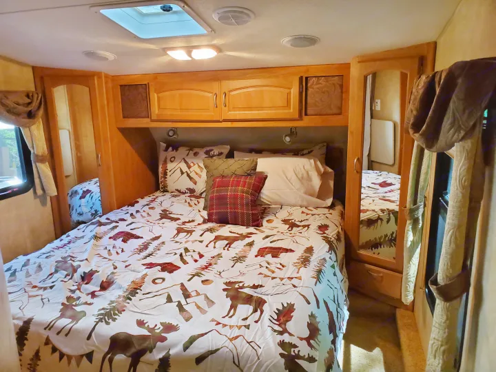 Cozy RV bedroom interior featuring a bed with nature-themed bedding, wood cabinets, and a skylight, perfect for an rv rental.. Forest River Wildcat 2009