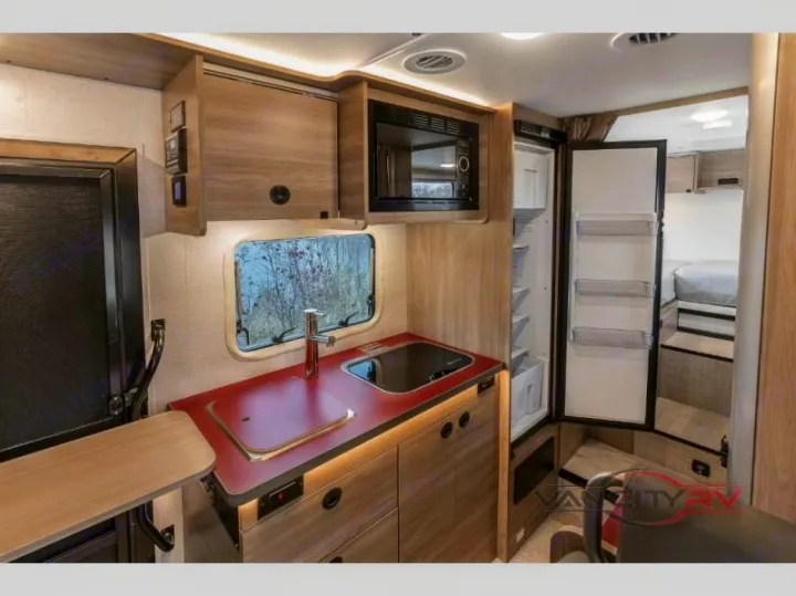 Compact RV rental interior featuring a kitchen with sink, stovetop, microwave & fridge, leading to a cozy bed area.. WINNEBAGO EKKO 2023