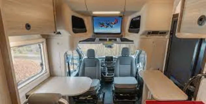 This RV rental interior features a dining area, cockpit, and a large TV, perfect for comfortable mobile living on your travels.. WINNEBAGO EKKO 2023
