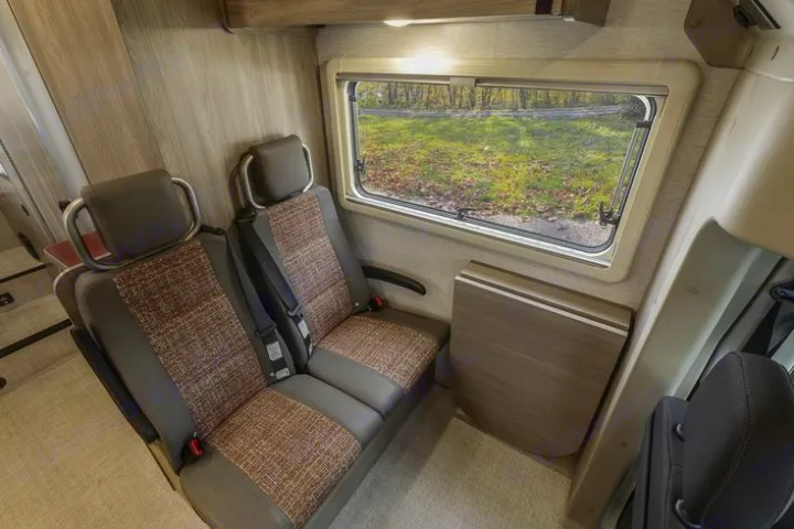 RV rental interior: cozy seating area with two passenger seats, a compact table, and a large window offering outdoor views.. WINNEBAGO EKKO 2023