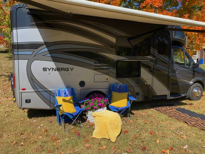 This RV rental features an extended awning, two chairs, and a blanket for comfortable outdoor living in vibrant fall colors.. Thor Synergy 2018
