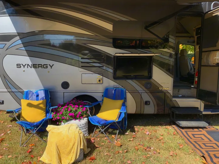 This RV rental offers a cozy outdoor camp setup: blue chairs, pink flowers, yellow cushions, and an exterior TV for comfort.. Thor Synergy 2018