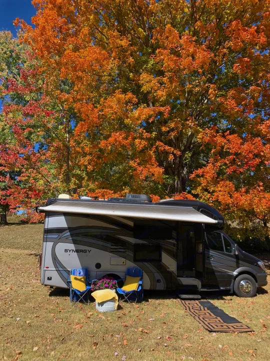 An RV rental nestled amidst brilliant fall foliage. Awning extended, chairs out – ready for autumn outdoor living.. Thor Synergy 2018