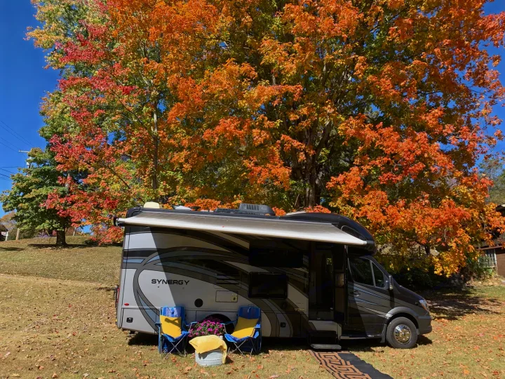 RV rental under vibrant autumn trees. Perfect fall camping setup with chairs and awning extended.. Thor Synergy 2018