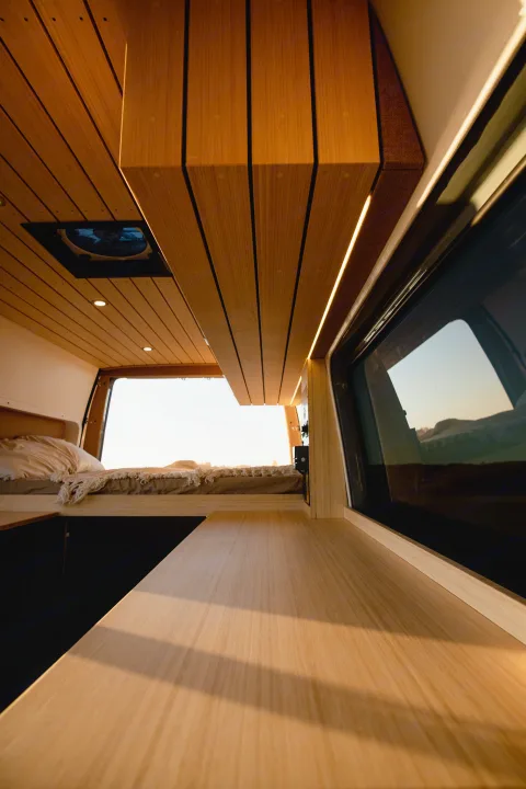 Cozy RV rental interior: light wood paneling, ambient LED lighting, and a comfortable bed for your next van adventure.. Mercedes-Benz Sprinter 2022