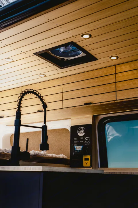 Modern RV rental interior featuring a stylish wooden slatted ceiling, a modern kitchen faucet, and a control panel for van systems.. Mercedes-Benz Sprinter 2022