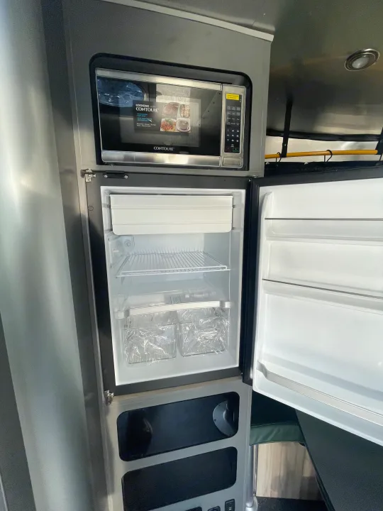 Compact RV kitchen featuring a Contoure microwave above an open refrigerator, ready for your next rv rental trip.. Airstream Basecamp 2022