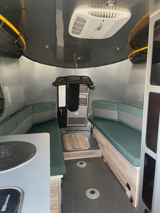 Inside a cozy rv rental: green cushioned seating, kitchen counter, AC, & wood accents. Ideal for your next trip!. Airstream Basecamp 2022