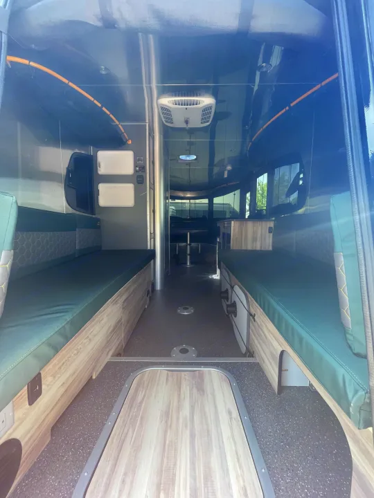 Spacious RV rental interior featuring comfortable green seating, wood-look accents, and a wide central living space.. Airstream Basecamp 2022