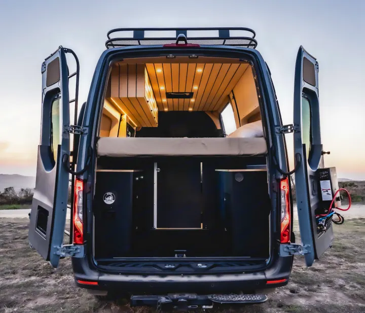 Explore this spacious rv rental camper van's rear view. Inside, find a comfy bed, wood-paneled ceiling with lights, & versatile storage.. Mercedes-Benz Sprinter 2022