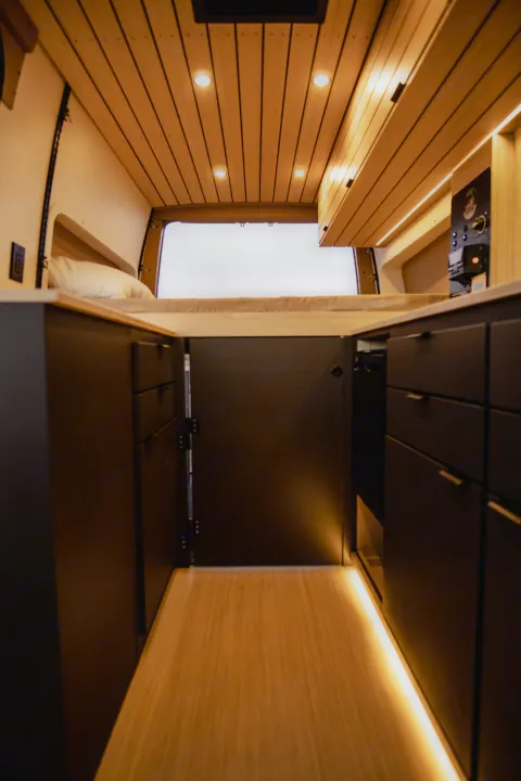 Explore a cozy RV rental interior, featuring a comfortable bed, smart storage, and warm wooden accents.. Mercedes-Benz Sprinter 2022