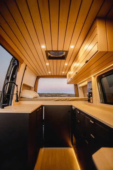Spacious RV rental interior with custom wood ceiling, ambient lighting, and a comfortable bed looking out to nature.. Mercedes-Benz Sprinter 2022