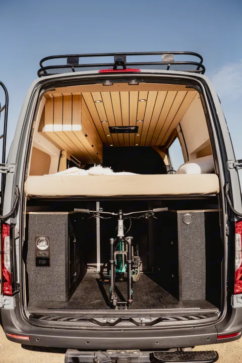 RV rental: View inside a custom camper van showing a raised bed & built-in mountain bike storage.. Mercedes-Benz Sprinter 2022