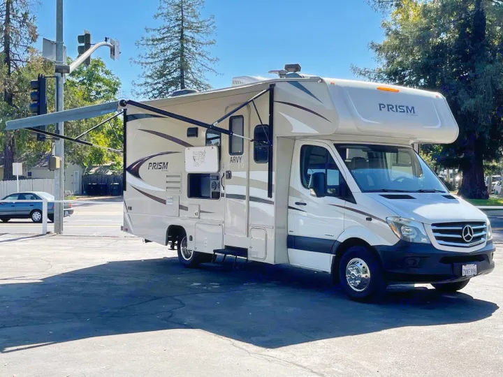 A modern tan & white Thor Prism Class C motorhome, an ideal rv rental, parked outdoors with its awning extended.. Forest River Coachmen Prism 2018