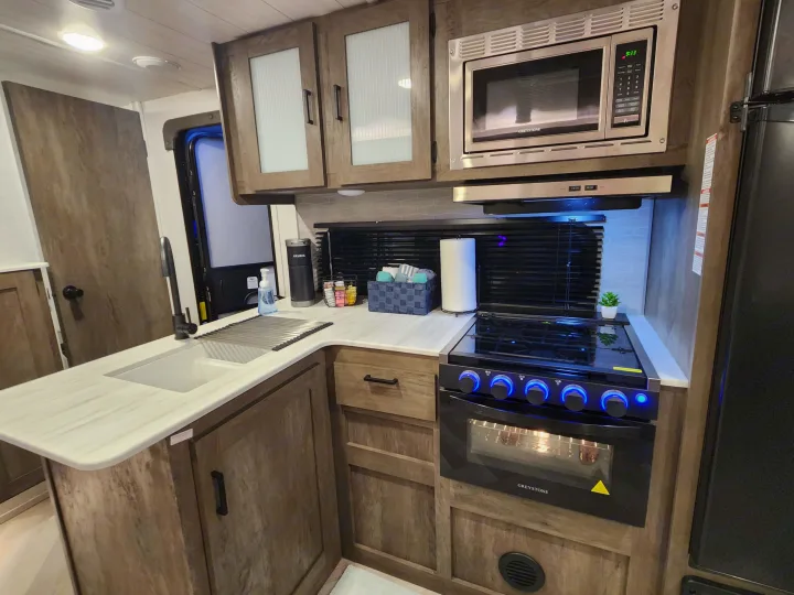 Spacious RV rental kitchen showcasing a modern stove, microwave, sink, and wood cabinets, ideal for travel cooking.. Forest River Salem Cruise Lite 2022