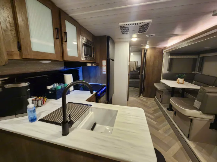 Bright rv rental interior featuring a well-equipped kitchen with a sink, stove, and microwave, plus a comfortable dinette.. Forest River Salem Cruise Lite 2022
