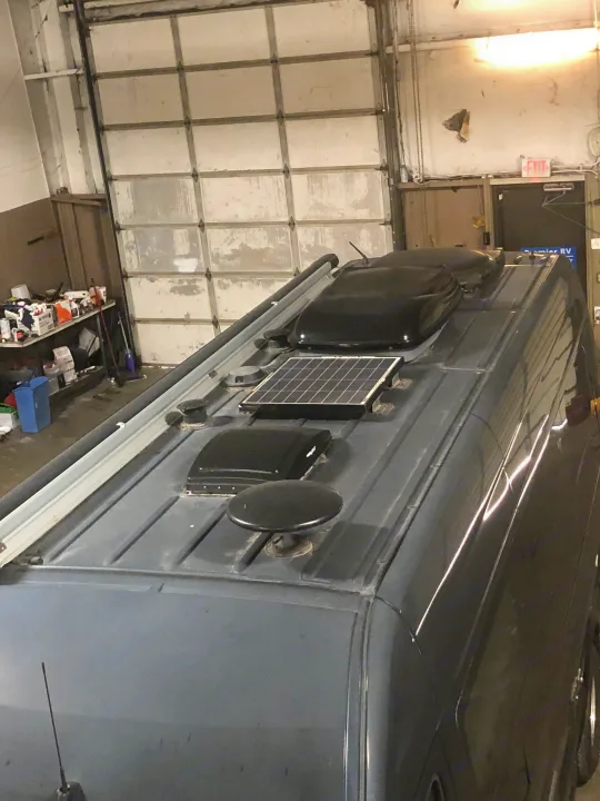 The roof of an RV rental van in a garage, featuring a solar panel, multiple vents, and other roof-mounted equipment.. Mercedes Sprinter 2015