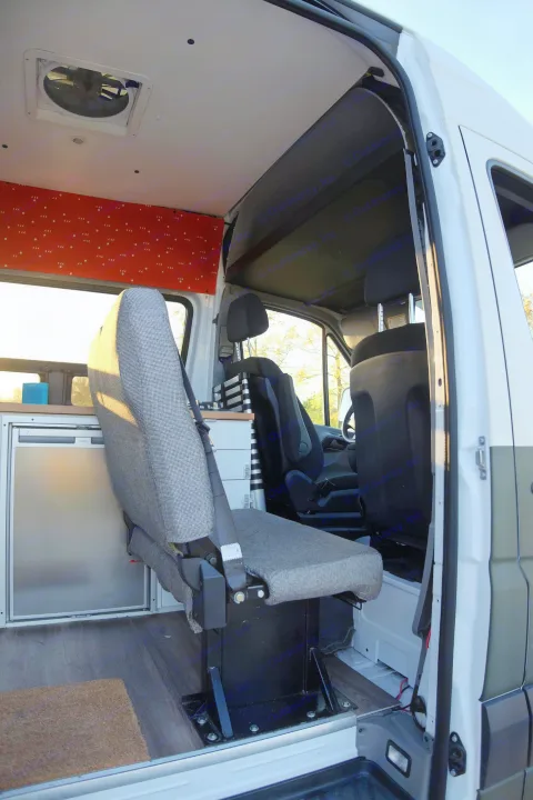 Inside an rv rental, a gray passenger seat is next to a Dometic fridge. Features a roof vent, wood floor, and custom wall paneling.. Mercedes-Benz Sprinter 2017