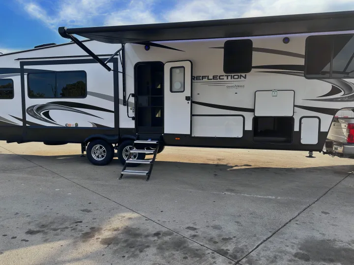 A large white and black Reflection Grand Design RV rental with an extended awning, open door, and steps, parked outside.. Grand Design Reflection 2022